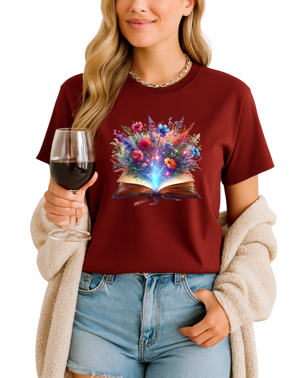 Person wearing a maroon t-shirt with a colorful book and flower design, holding a glass of red wine.