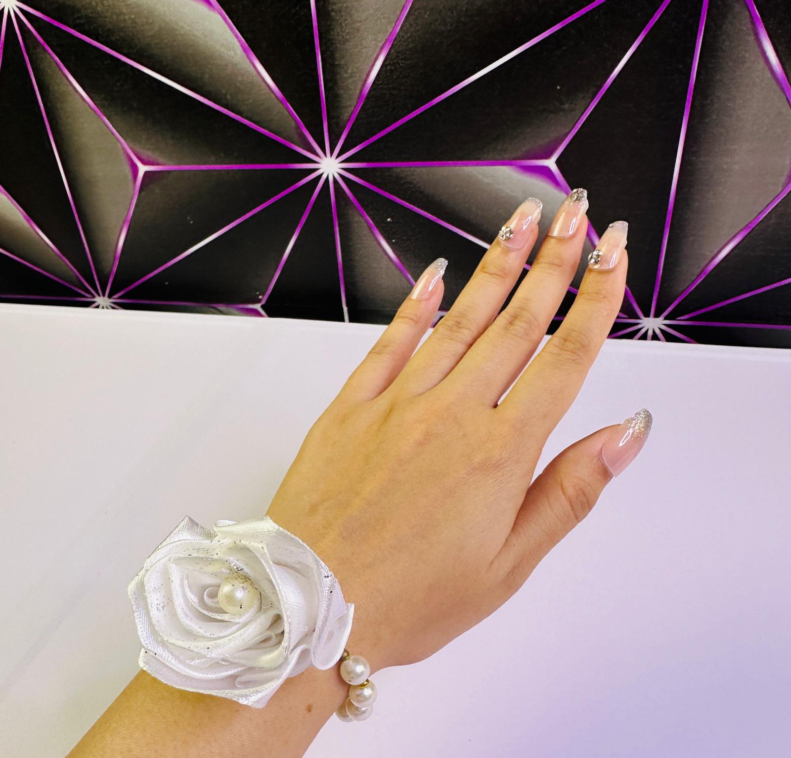 Hand wearing a white wrist corsage against a geometric black and purple background