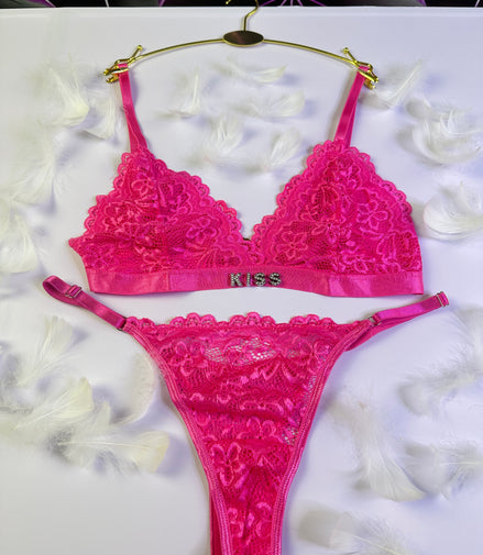 Pink lace lingerie set with 'Kiss' branding on a white surface.